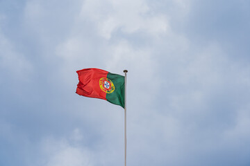 Portuguese flag on a flagpole against the sky with storm clouds.