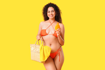 Beautiful young African-American woman in swimsuit with bottle of sunscreen cream on yellow...