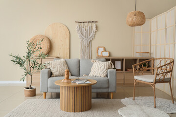 Interior of light living room with grey sofa, coffee table, chair and olive tree