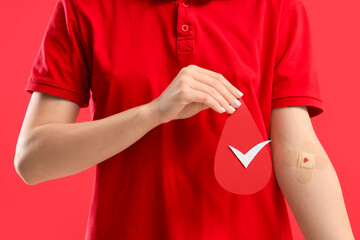 Female blood donor with applied patch and paper drop on red background, closeup