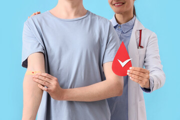 Male blood donor and doctor with paper drop on blue background, closeup