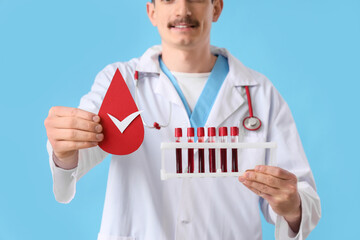 Male doctor with paper blood drop and test tubes on blue background, closeup