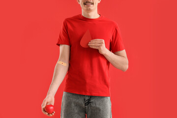 Male blood donor with paper drop and grip ball on red background