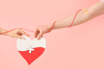 People with paper heart and tube on pink background. Blood donation concept