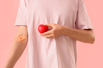 Male blood donor with applied patches and grip ball on pink background, closeup