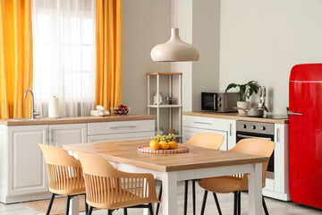 Interior of modern kitchen with white counters, dining table, red fridge, chairs and lamp