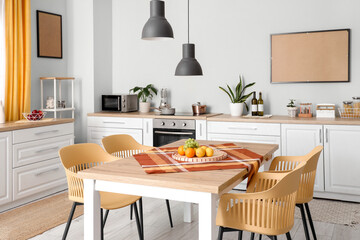 Interior of beautiful kitchen with white counters, dining table, fruits, chairs and lamps