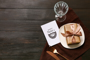 Festive decorated table setting with gift box and greeting card on black wooden background. Father...