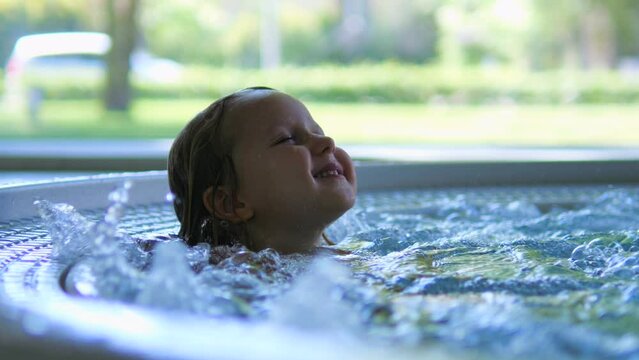 Close-up face satisfied child bathing in water with bubbles in jacuzzi. Water gently washes face, delivering true pleasure. Girl feels relaxed and peaceful in seething water jacuzzi flowing around.