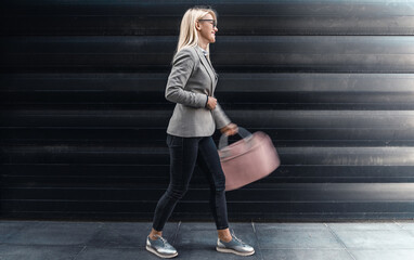 Smiling businesswoman holding laptop bag walking on the street.