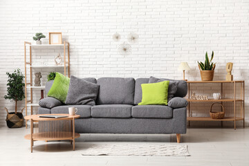Stylish interior of living room with comfortable sofa, coffee table, shelving unit and pillows