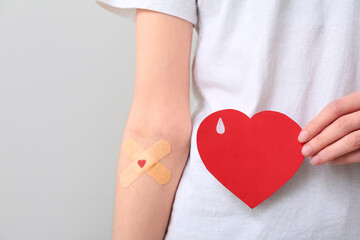 Woman with applied medical patches and paper heart on grey background. World Blood Donor Day