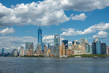 Fototapeta premium New York, NY, USA - August 1, 2023: Panorama, Manhattan south Hudson river shoreline, and southern tip featuring urban jungle of skyscrapers under blue cloudscape. Battery Park ads green 