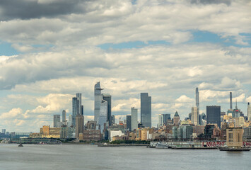 Naklejka premium New York, NY, USA - August 1, 2023: 30 Hudson Yards and other skyskrapers under blue cloudscape. From Chelsey golfclub to Holland Tunnel ventilation shaft 2. Skyscraper city skyline and Hudson river p