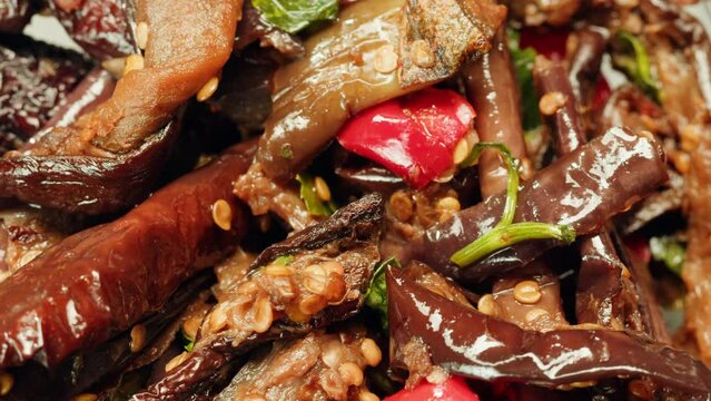 Close-up of fermented eggplants with red sweet pepper and mustard on plate. Preservation of vegetables in glass jars. Fermentation preserved aubergine with hot chilli peppers and greens. 