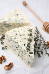 Tasty blue cheese with thyme, walnuts and honey dipper on white table, closeup