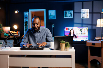 African american man mixing on DJ turntables, doing music production tutorial for his online...