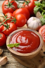 Tasty ketchup, fresh tomatoes, basil and spices on wooden table