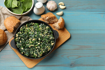 Tasty spinach dip with eggs in dish served on light blue wooden table, flat lay. Space for text