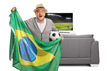 Excited soccer fan holding a football and a Brazilian flag and watching a game on tv