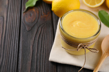 Delicious lemon curd in glass jar, fresh citrus fruit and spoon on wooden table, space for text