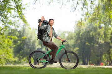 Fototapeta premium Full length profile shot of a young man with a backpack riding a bicycle in a park