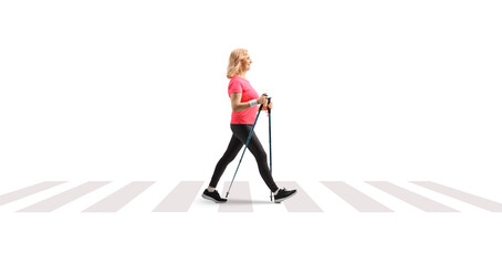 Full length profile shot of a middle aged woman walking with trekking poles at a pedestrian crossing