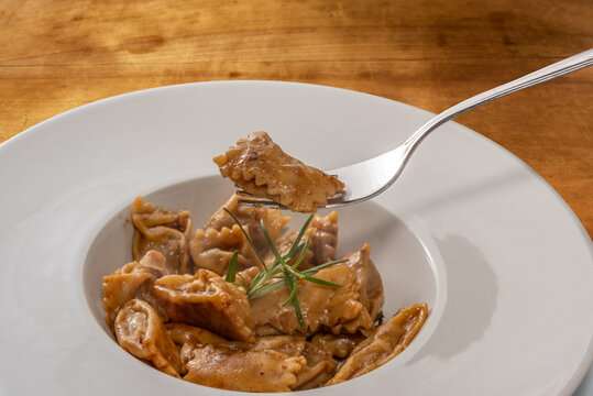 Agnolotti del Plin served with roast sauce, Plin egg pasta ravioli over fork on white plate on wooden table