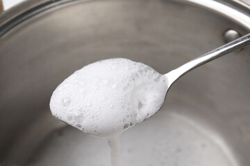 Chemical reaction of vinegar and baking soda in spoon over saucepan, closeup