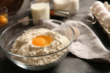 Making dough. Flour with egg yolk in bowl on grey table, closeup