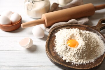 Making dough. Pile of flour with yolk, rolling pin and eggs on white wooden table, closeup
