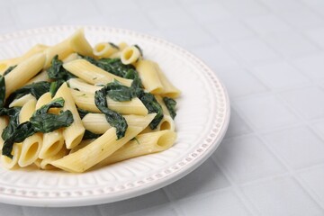 Tasty pasta with spinach and sauce on white tiled table, closeup