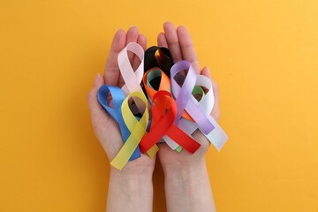 Woman with many colorful awareness ribbons on orange background, top view