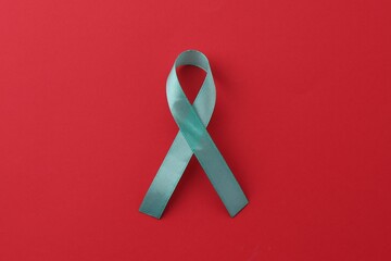 Turquoise awareness ribbon on red background, top view