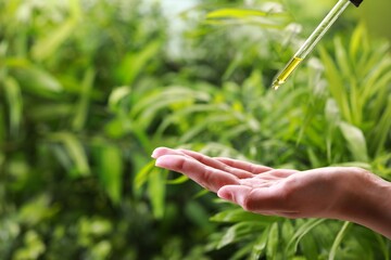 Woman dripping essential oil from pipette outdoors, closeup