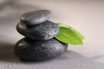 Wet spa stones and green leaves on grey background