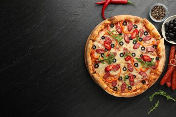 Tasty pizza and ingredients on black table, top view. Space for text
