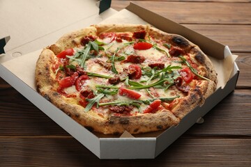 Tasty pizza with cheese, tomato and arugula in cardboard box on wooden table