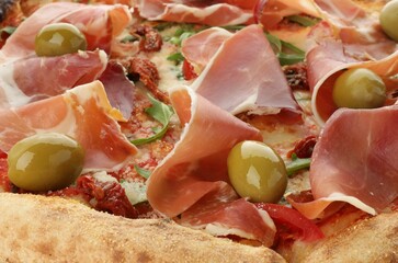 Tasty pizza with cured ham, olives and sun-dried tomato as background