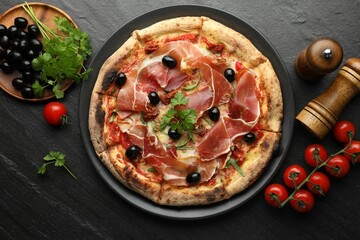 Tasty pizza with cured ham, olives, tomatoes and parsley on black table, top view