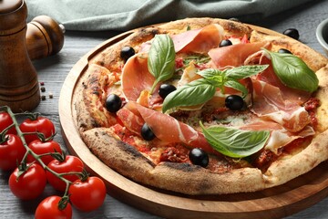 Tasty pizza with cured ham, olives, tomatoes and basil on gray wooden table, closeup