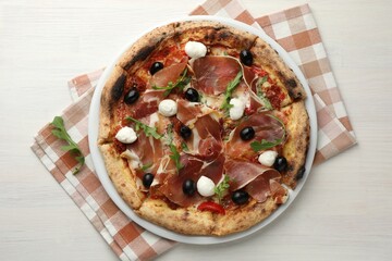Tasty pizza with cured ham, olives, mozzarella cheese, sun-dried tomato and arugula on light wooden table, top view