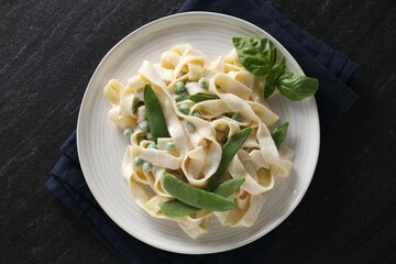Delicious pasta with green peas and creamy sauce on black table, top view