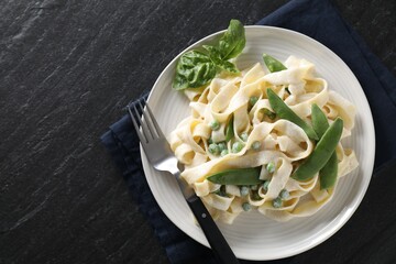 Delicious pasta with green peas and creamy sauce on black table, top view. Space for text
