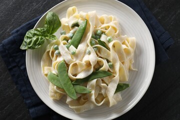 Delicious pasta with green peas and creamy sauce on black table, top view