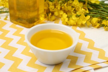 Rapeseed oil in bowl and beautiful yellow flowers on table, closeup