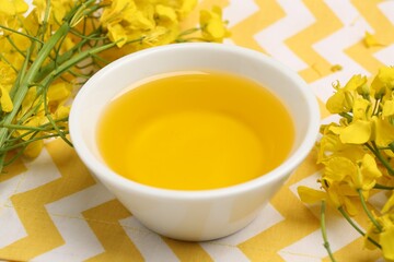 Rapeseed oil in bowl and beautiful yellow flowers on table, closeup