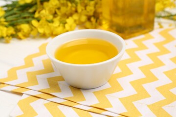 Rapeseed oil in bowl and beautiful yellow flowers on table
