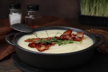 Delicious potato soup with bacon and microgreens in bowl served on wooden table, closeup