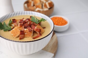 Delicious lentil soup with bacon and parsley in bowl on white tiled table, closeup